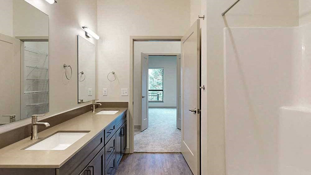 a bathroom with a double sink, mirror, and a door leading to a walk-through closet