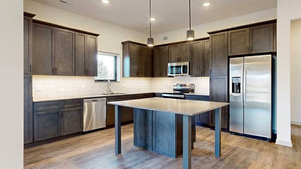 a modern L-shaped kitchen with dark cabinets, stainless steel appliances, quartz counter tops, and a central island table