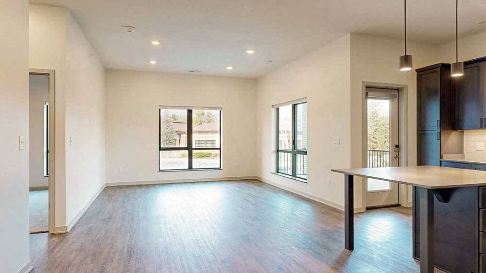 a spacious living room with hardwood floors and two large windows