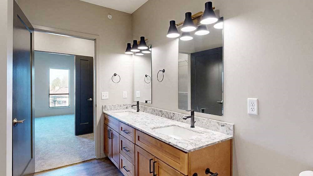 a bathroom with a double vanity sink, two mirrors, and a door to the walk-through closet