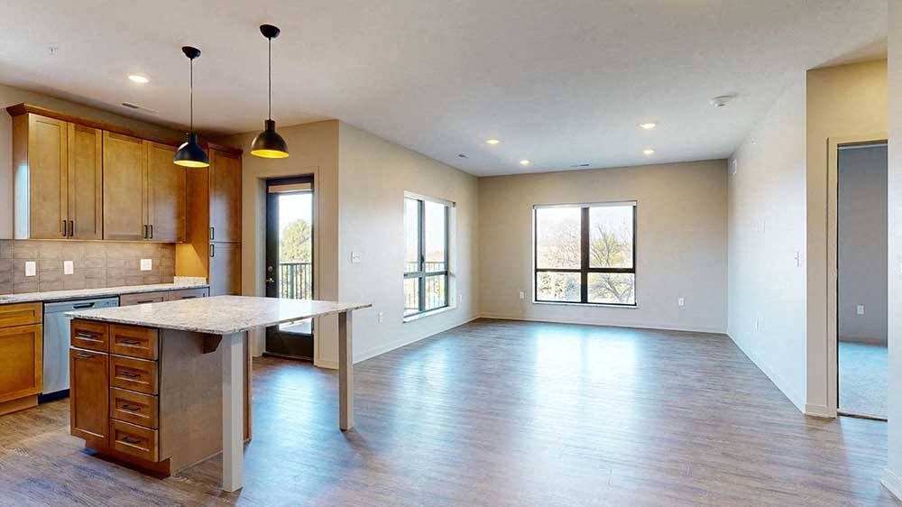 a spacious kitchen with wooden cabinets and a large island next to an open living room with two large windows