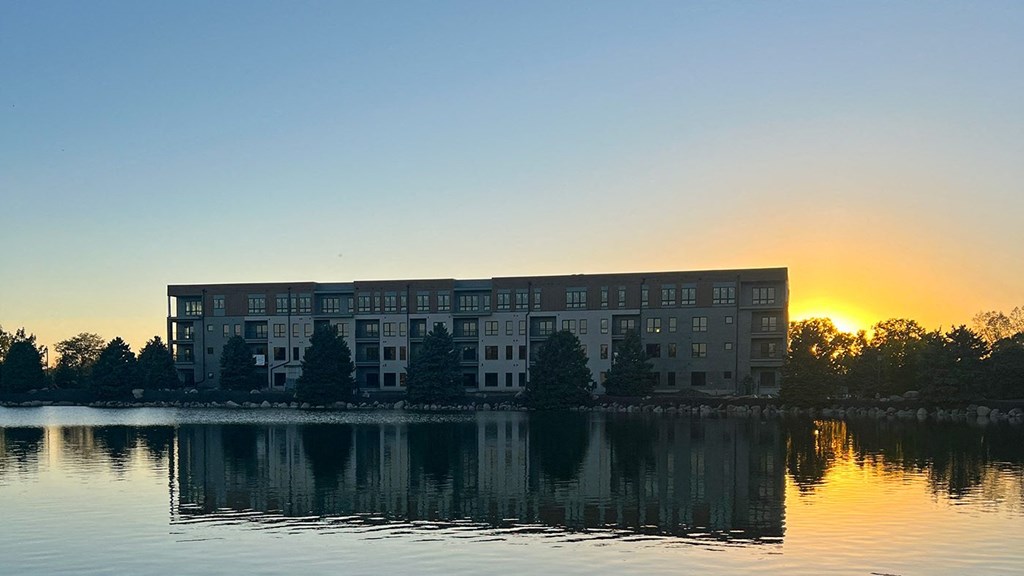 a building on the lake at sunset with the sun setting behind it