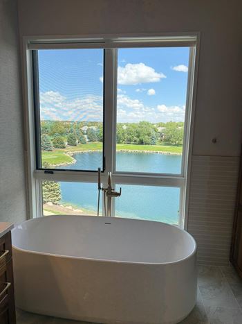 A white bathtub is in a bathroom with a window overlooking a large pond