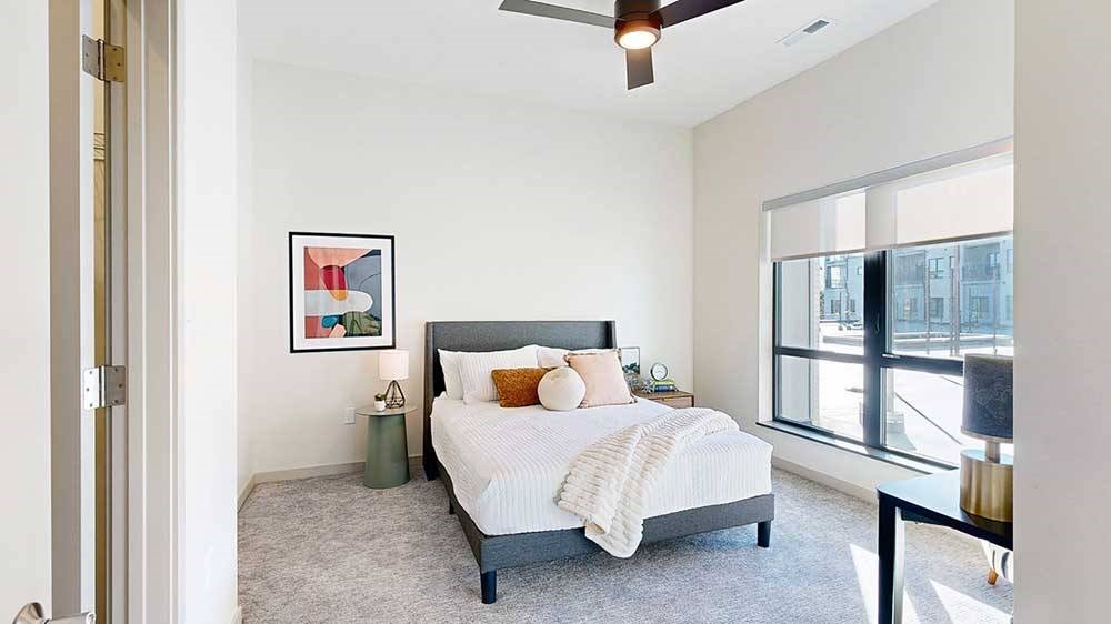 a view of the bedroom from the doorway, furnished with modern decor, a ceiling fan, and a large window overlooking the courtyard