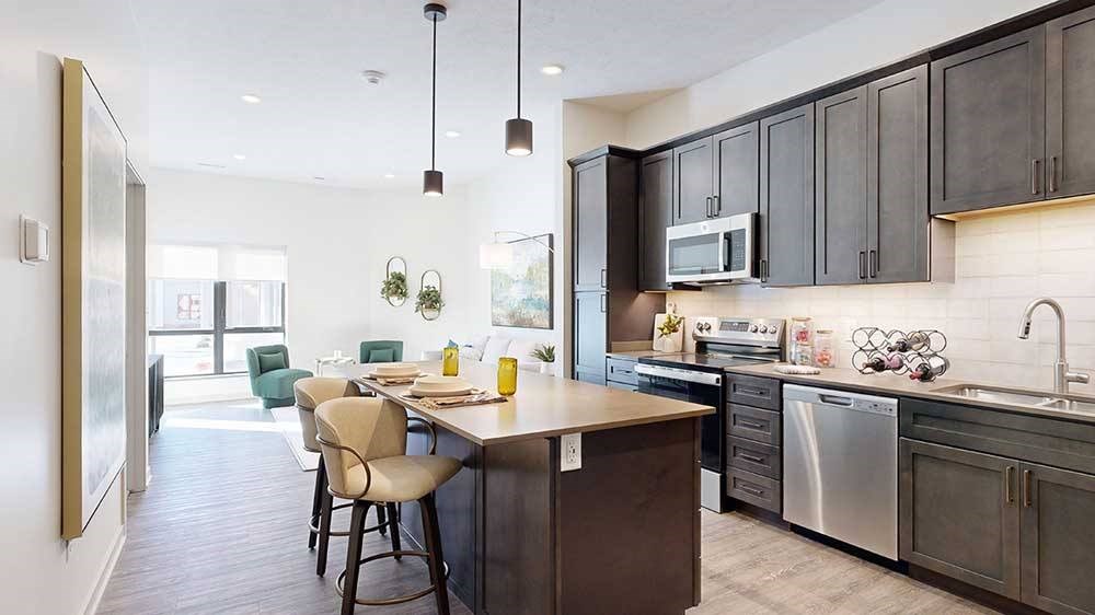 a modern kitchen with a stainless steel appliances, quartz countertops, a light tile backsplash, dark wooden cabinets, and a large central island