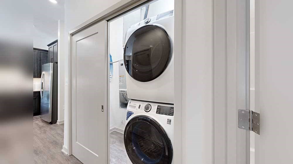 a white and black stackable full-size washer and dryer in a double door closet in the front hallway
