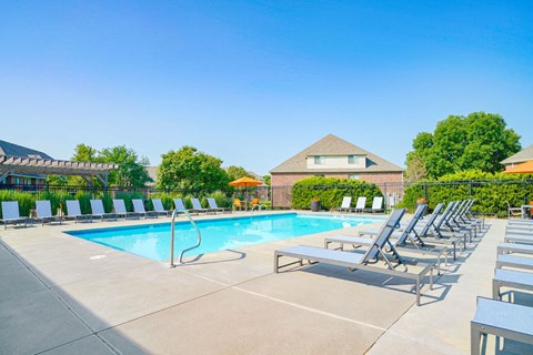a swimming pool surrounded by rows of lounge chairs with an apartment building in the background