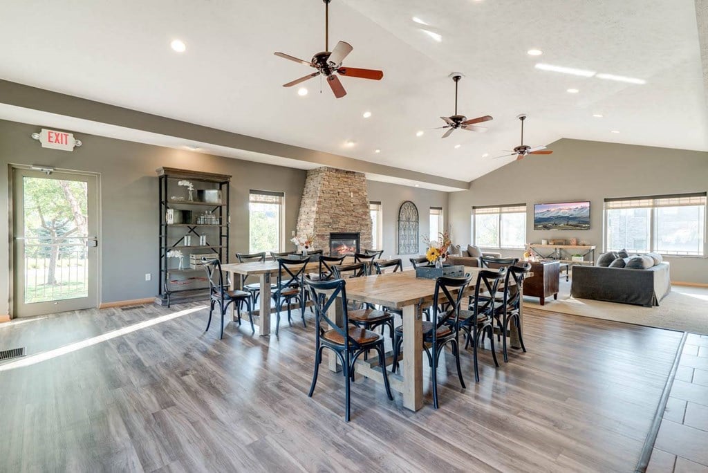 a modern community clubhouse with hardwood floors, large tables, a fireplace, and a tv area
