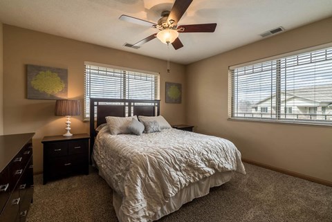 a bedroom with a queen bed, dark wood furniture, and a ceiling fan