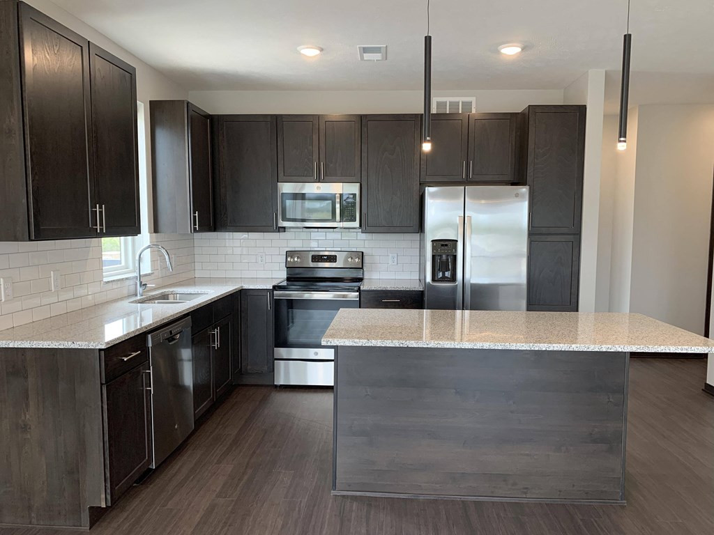 Large kitchen with warm dark brown cabinets, stainless steel appliances, and an island
