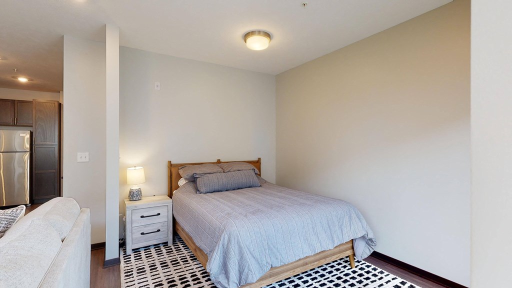 a studio with a bed and bedside table with lamp