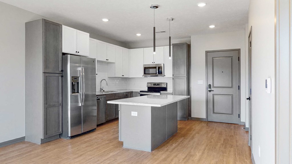 Slate finish kitchen with two tone cabinets, light hard wood style flooring, granite counter tops, and white back splashes in the Bliss floor plan at Haven at Uptown in Lincoln, NE