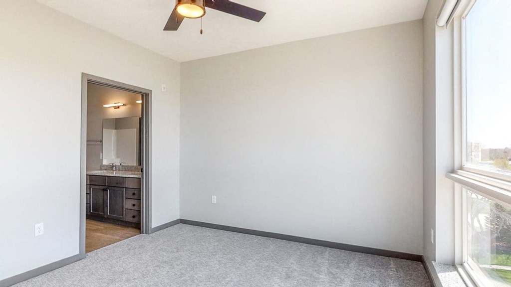 Master bedroom with large windows providing natural light, ceiling fan, and attached bathroom at Haven at Uptown in Lincoln, NE