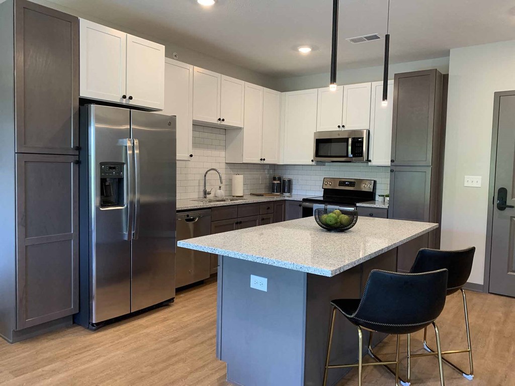 apartment kitchen with stainless steel appliances, white upper cabinets, warm grey lower cabinets, and white counters