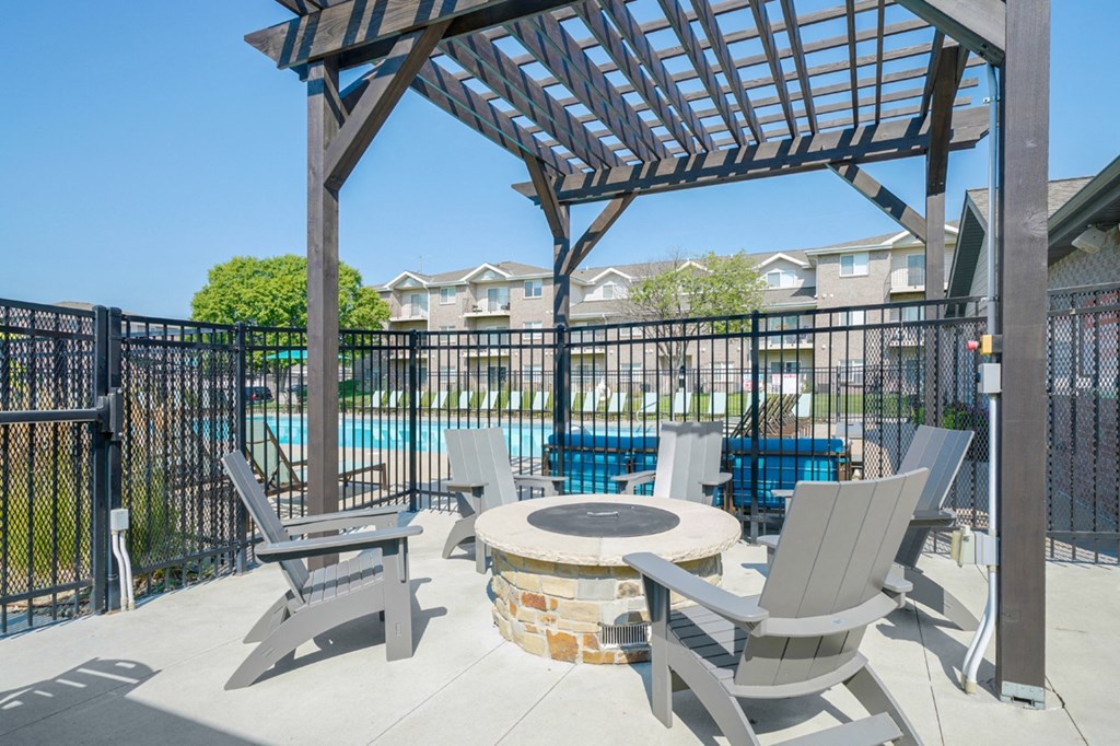a poolside lounge space with Adirondack chairs surrounding a fire pit under a pergola