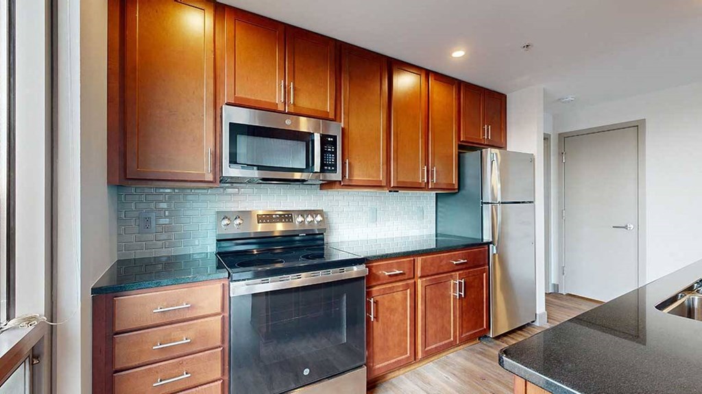 a modern kitchen with brown wooden cabinets, stainless steel appliances, black granite countertops, and a tile backsplash
