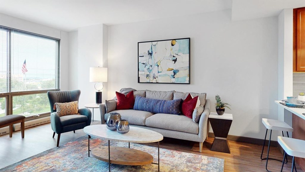 A living room with a grey couch, a black chair, a wooden coffee table, and large windows