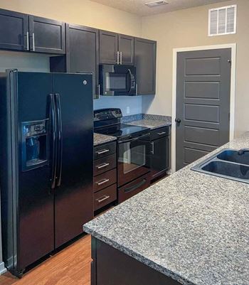 a kitchen with dark wooden cabinets, granite countertops, and black appliances
