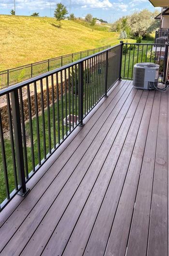 a wooden deck with a black metal railing looking over a green space