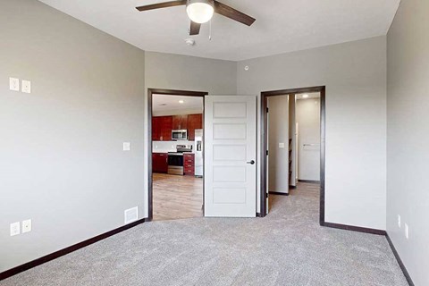 A carpeted bedroom with a ceiling fan and a walk-in closet and attached bathroom.