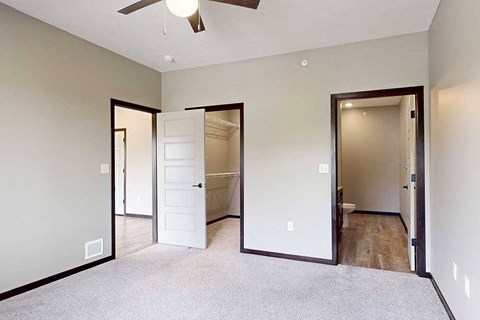 A carpeted bedroom with a ceiling fan, a walk-in closet, and an attached bathroom.
