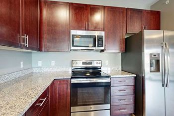 A modern kitchen with wooden cabinets, granite counters, and stainless steel appliances.