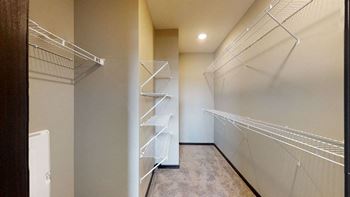 A walk-in closet with white shelving and a carpeted floor.
