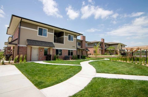 A villa-style apartment building with a green lawn in front of it, and a fenced in pool nearby.