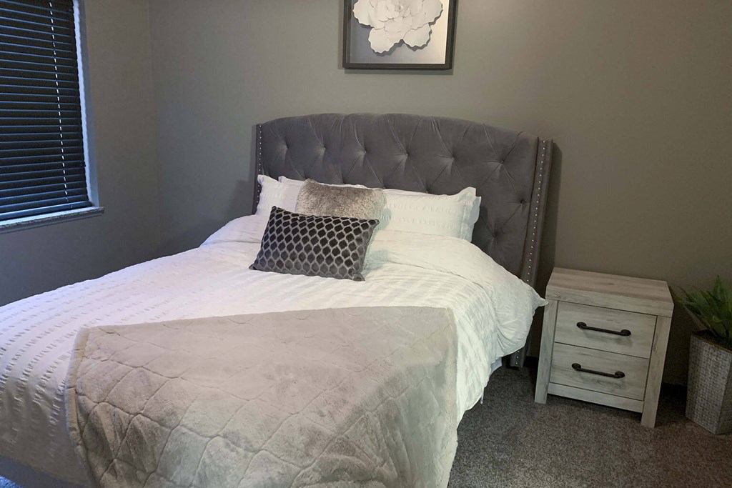 a bed with a white comforter and pillows in a small bedroom