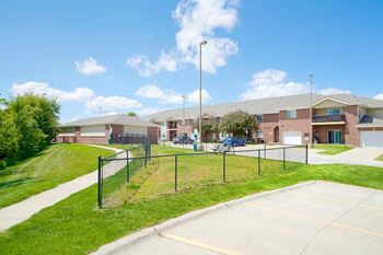 a fenced in dog park with open green space to let your dog off-leash in front of an apartment building