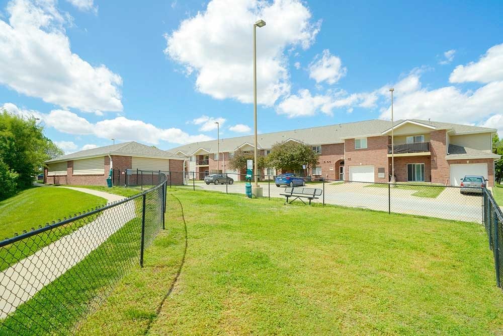 a fenced in dog park with open green space to let your dog off-leash, with a bench