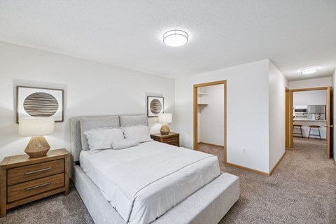 A bedroom with a large bed and two nightstand with lamps, and attached walk-in closet