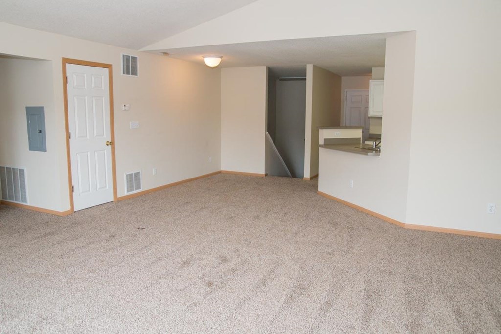 an empty living room with a door to the kitchen