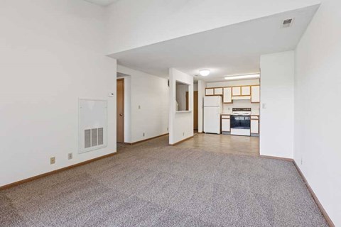 A spacious living room with a grey carpet and white walls.