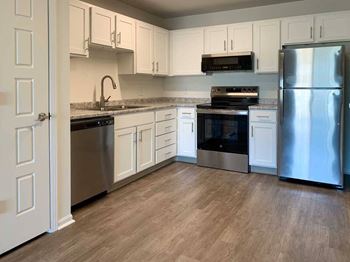 an updated L-shape kitchen with white cabinets, stainless steel appliances, and hardwood flooring