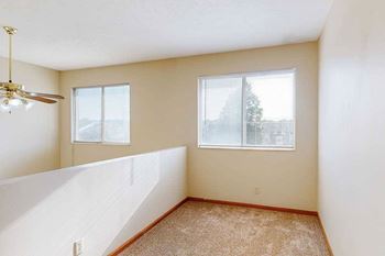A carpeted loft bedroom with a view open to below, two bright windows, and a ceiling fan.