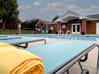 apartment swimming pool with two light blue lounge chairs a clubhouse in the background
