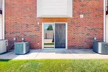 A red brick apartment building with a patio and a sliding glass door into a living room.