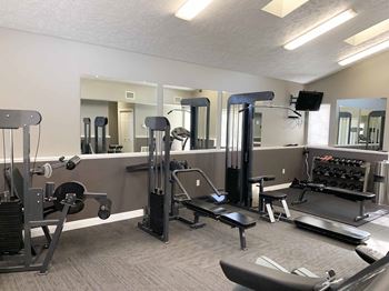 a gym with equipment and mirrors in apartment clubhouse