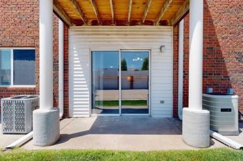 A patio with two pillars, and a sliding glass door to a living room.