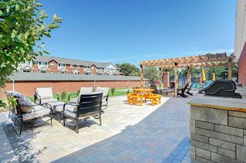 An outdoor patio with social seating areas, a picnic table, grilling stations, a fire pit, and a pergola.