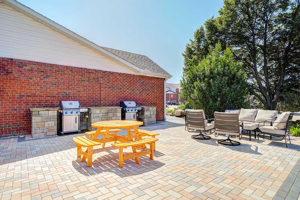 A round picnic table on a patio in front of two grilling stations.