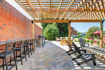 A patio with a pergola covering bar top seating and a fire pit with chairs around it.