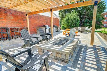 A patio with a pergola covering a fire pit with surrounding chairs.
