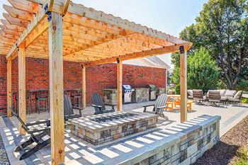 A wooden pergola over a patio with black chairs and a stone fire pit.