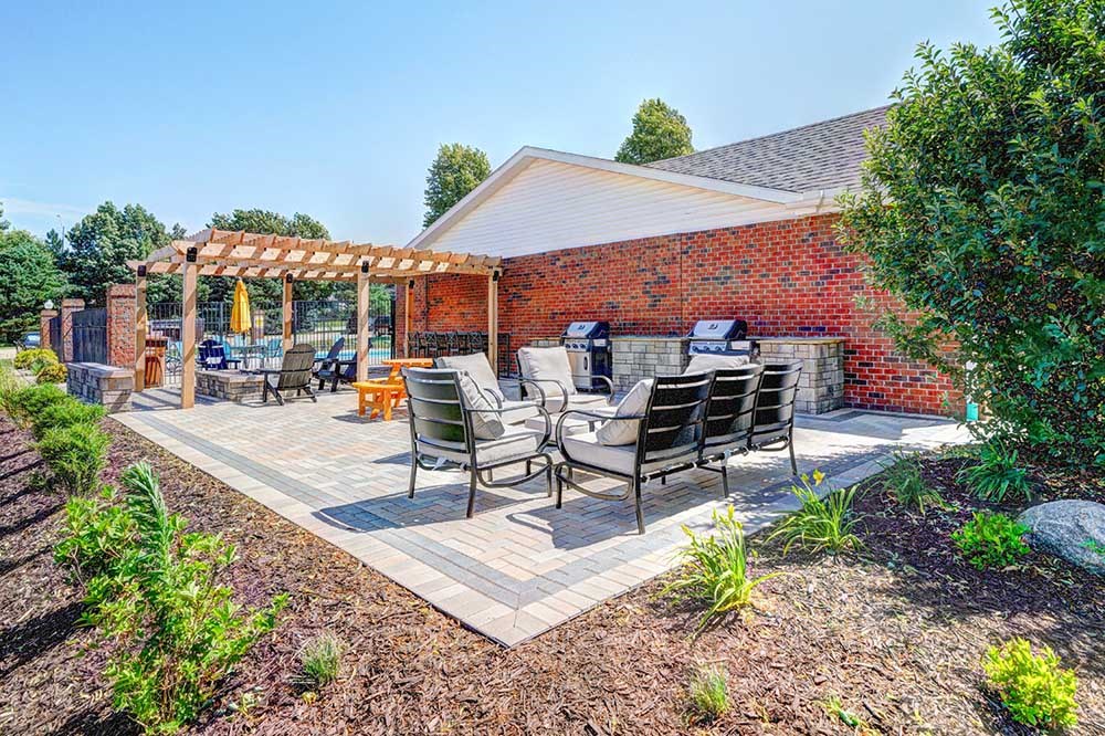 An outdoor patio with social gathering seating, a picnic table, grilling stations, a fire pit, and a pergola.