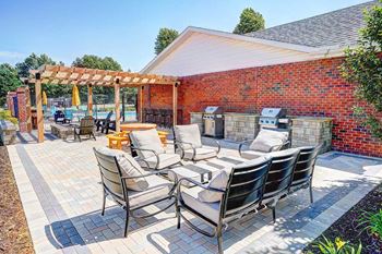 An outdoor patio with social seating areas, a picnic table, grilling stations, a fire pit, and a pergola.