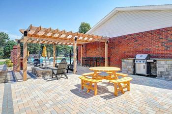 An outdoor patio with social seating areas, a picnic table, grilling stations, a fire pit, and a pergola.