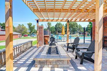 A wooden pergola over a stone fire pit with black chairs around it.