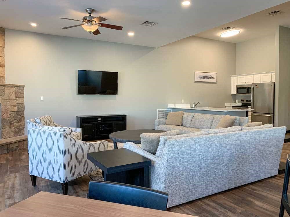 a clubhouse living room with a grey couch, a black television, and a stone fireplace
